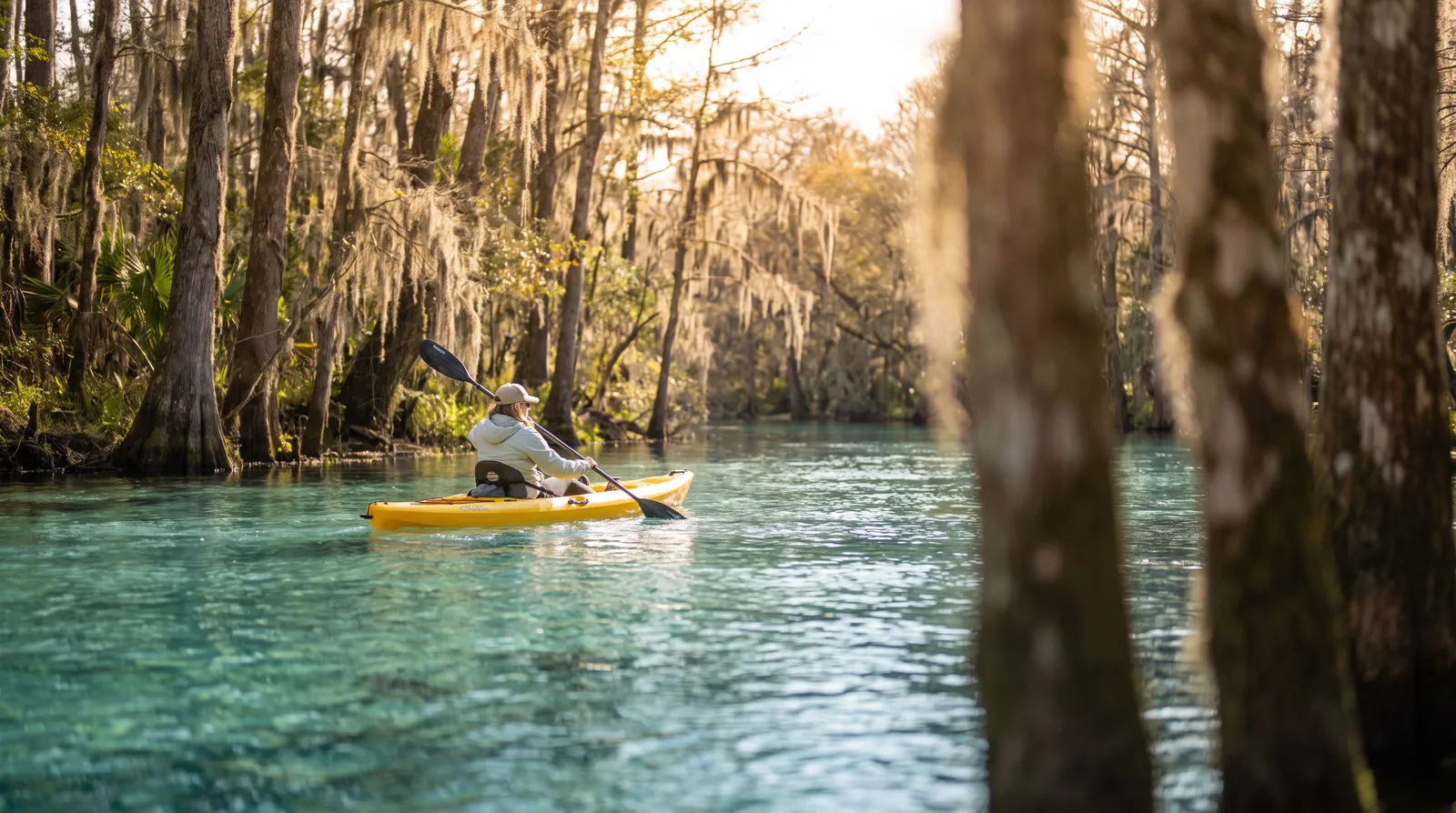 A kayaker paddling clear spring water past cypress trees on the Weeki Wachee River on a bright Florida morning